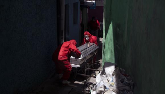 Los trabajadores de una funeraria vestidos con trajes de bioseguridad llevan el cuerpo de un hombre de 75 años que murió, presuntamente víctima de coronavirus COVID-19, en la puerta de su casa mientras pedía ayuda en la comunidad de La Fosa, en San Salvador. (Foto por Yuri CORTEZ / AFP).