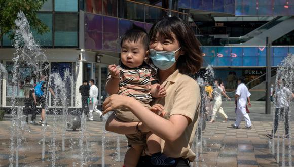 Una mujer sostiene a su hijo fuera de un centro comercial en el Día Internacional del Niño en Beijing, el 1 de junio de 2021. (NICOLAS ASFOURI / AFP).