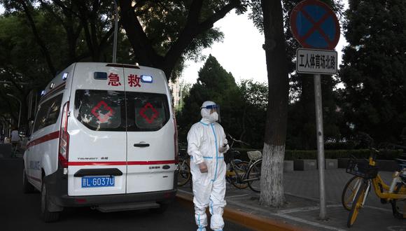 Un trabajador que usa un traje protector para ayudar a protegerse contra el COVID-19 se para frente a una ambulancia estacionada en una calle de Beijing.