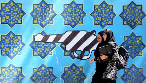 Dos mujeres pasan junto a un mural dibujado en la pared de la antigua embajada de Estados Unidos en la capital de Irán, Teherán. (Foto de ATTA KENARE / AFP).