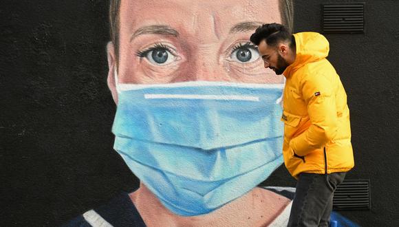 Un peatón pasa junto a un grafiti del artista @akse_p19, que representa a una enfermera del NHS con bata médica y una máscara facial, pero con un halo de ángel sobre su cabeza, en Manchester, noroeste de Inglaterra. (Foto de Oli SCARFF / AFP).