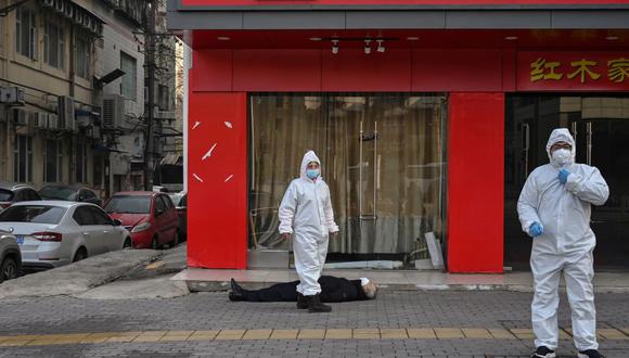 Esta foto tomada el 30 de enero de 2020 muestra a funcionarios con trajes protectores junto a un anciano que murió en una calle cerca de un hospital en Wuhan, en plena pandemia de coronavirus. (Foto de Hector RETAMAL / AFP).