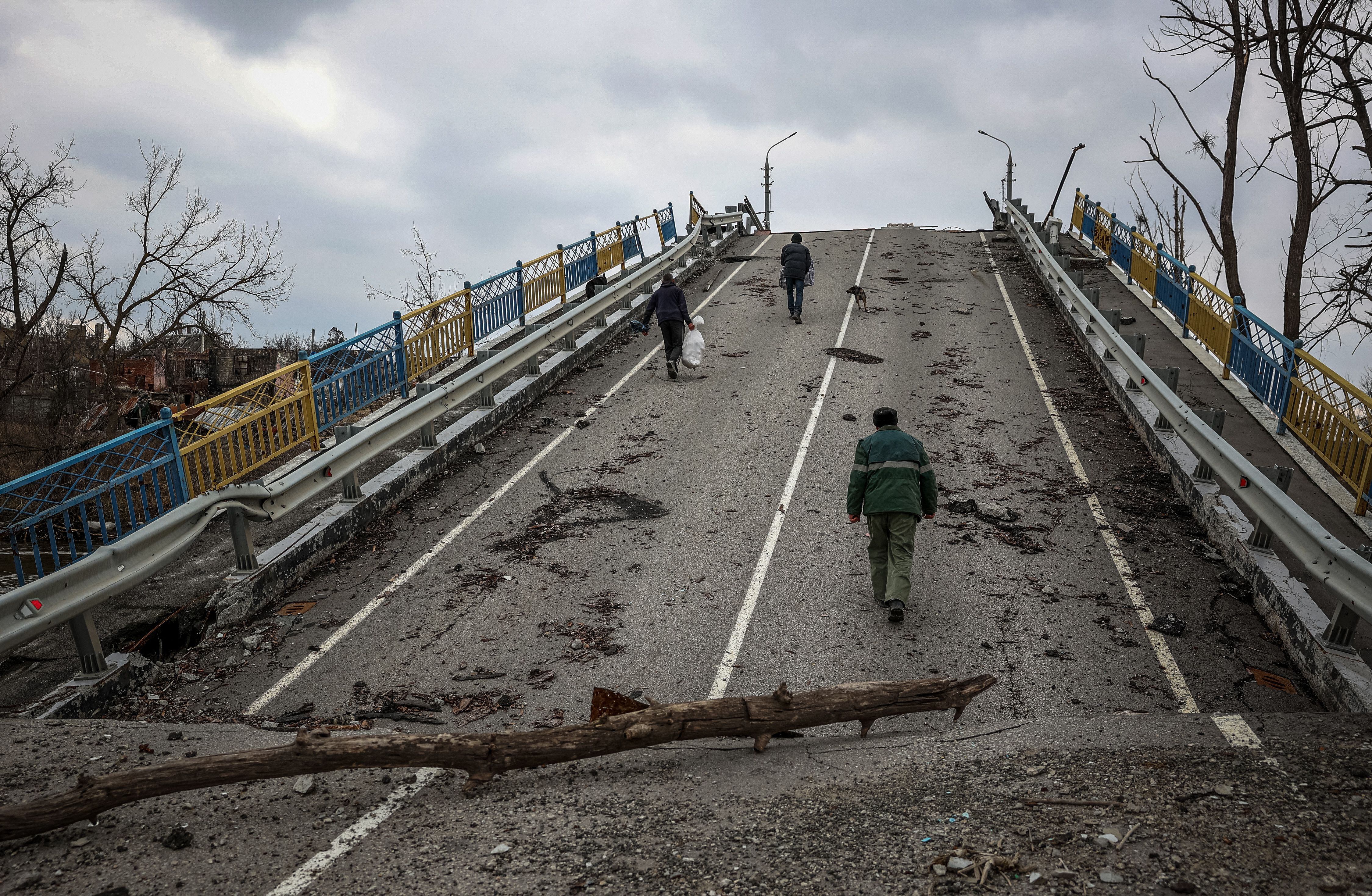 Los residentes locales del pueblo de Bohorodychne caminan sobre un puente destruido por un bombardeo ruso el 10 de marzo de 2023. (Foto de ANATOLII STEPANOV / AFP).