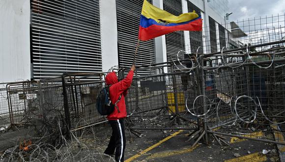 Un manifestante ondea una bandera de Ecuador mientras policías montan guardia en los alrededores de la Asamblea Nacional en Quito el 25 de junio de 2022. (MARTIN BERNETTI / AFP).