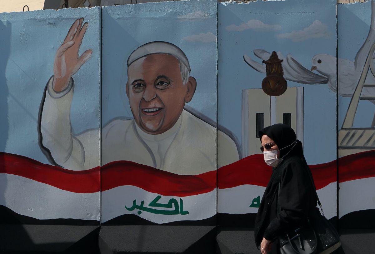 Una mujer pasa junto a un mural que representa al papa Francisco en un muro de concreto colocado por las fuerzas de seguridad iraquíes para rodear la Iglesia Nuestra Señora de la Salvación durante los preparativos para la visita del sumo pontífice a Bagdad, Irak. (AP/Khalid Mohammed).