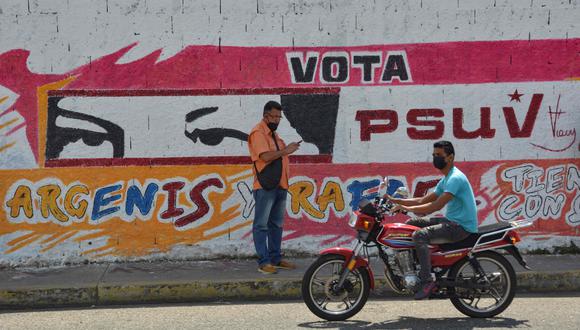 Un motociclistas conduce al frente de un grafiti de Argenis Chavez en Barinas. (Foto: AFP)
