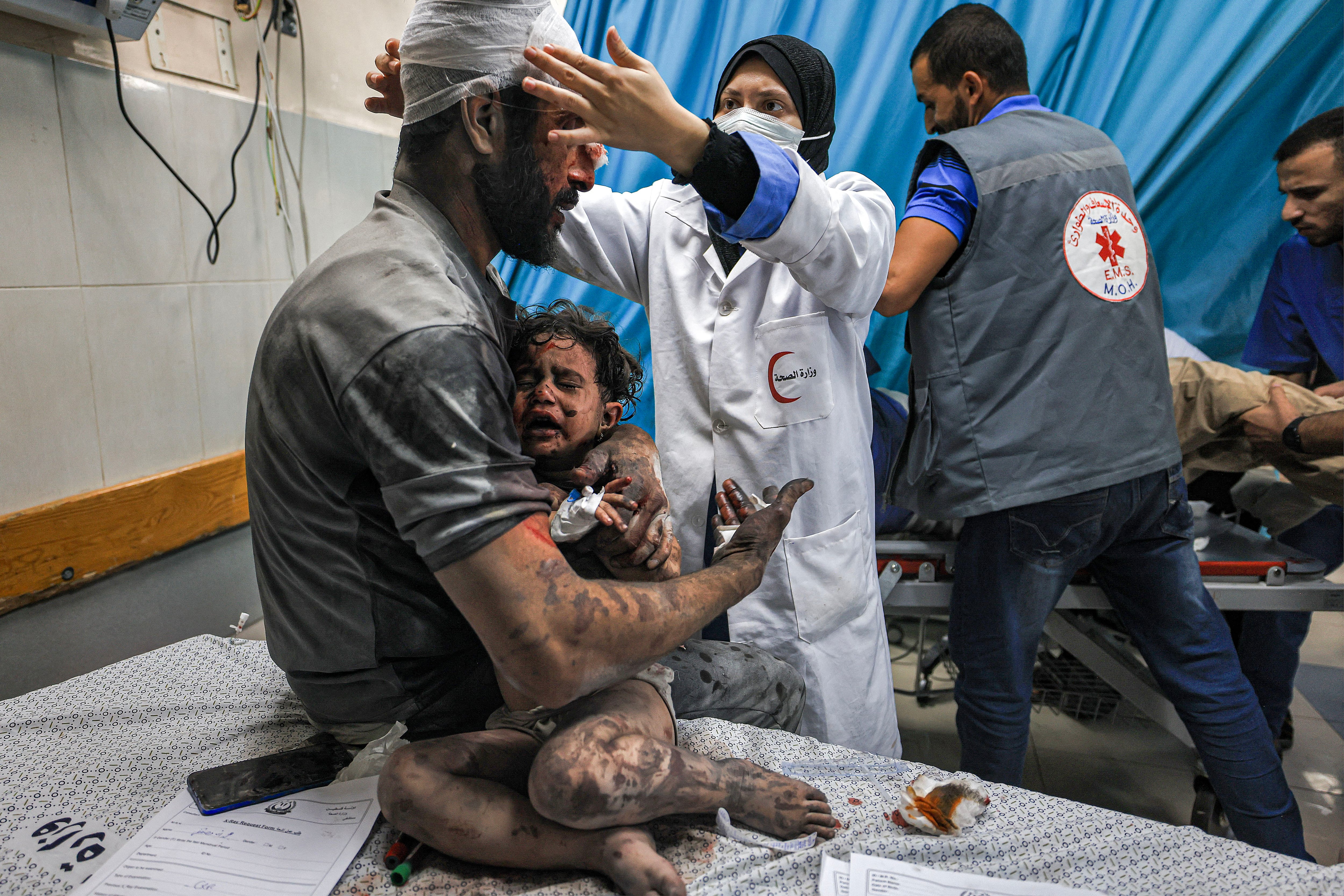 An injured man holds an injured child undergoing treatment in the trauma room of the Nasser hospital in Khan Yunis, south of the Gaza Strip, following an Israeli bombardment.  (Photo by Mahmud HAMS/AFP).