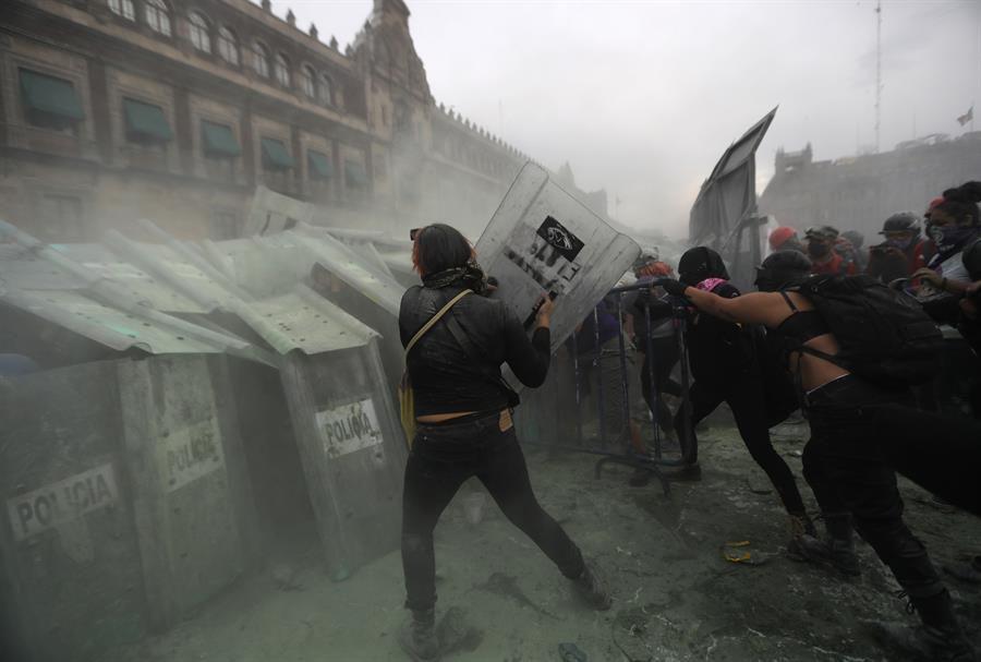 Mujeres activistas arremeten contra las policías que custodian el perímetro del Palacio Nacional de México. (EFE/Sáshenka Gutiérrez).