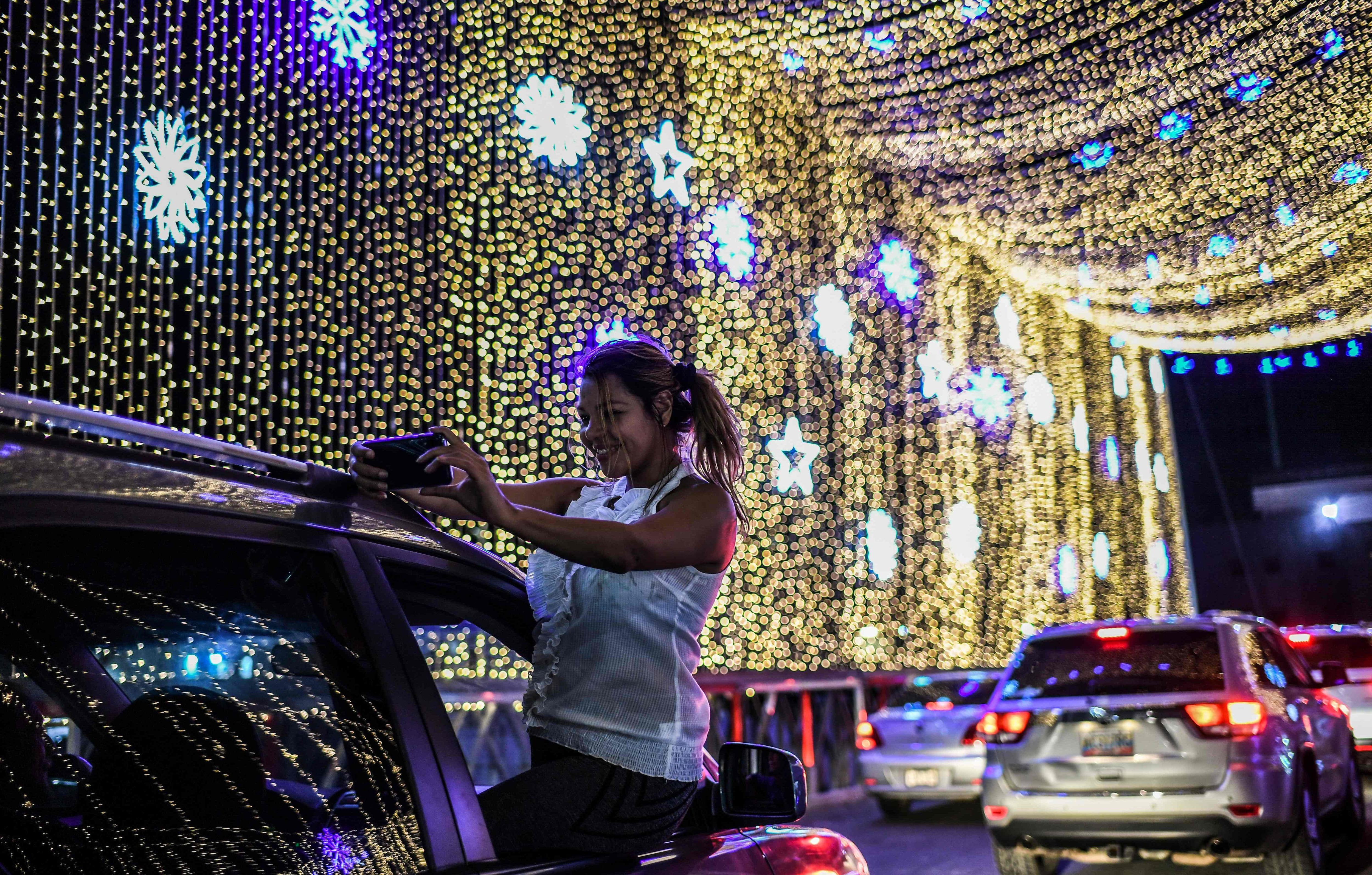 Una mujer sale por la ventana del auto para tomarse un selfie con las luces de Navidad colocadas en el puente sobre el río Guaire en Caracas, Venezuela. (AFP / Yuri CORTEZ).