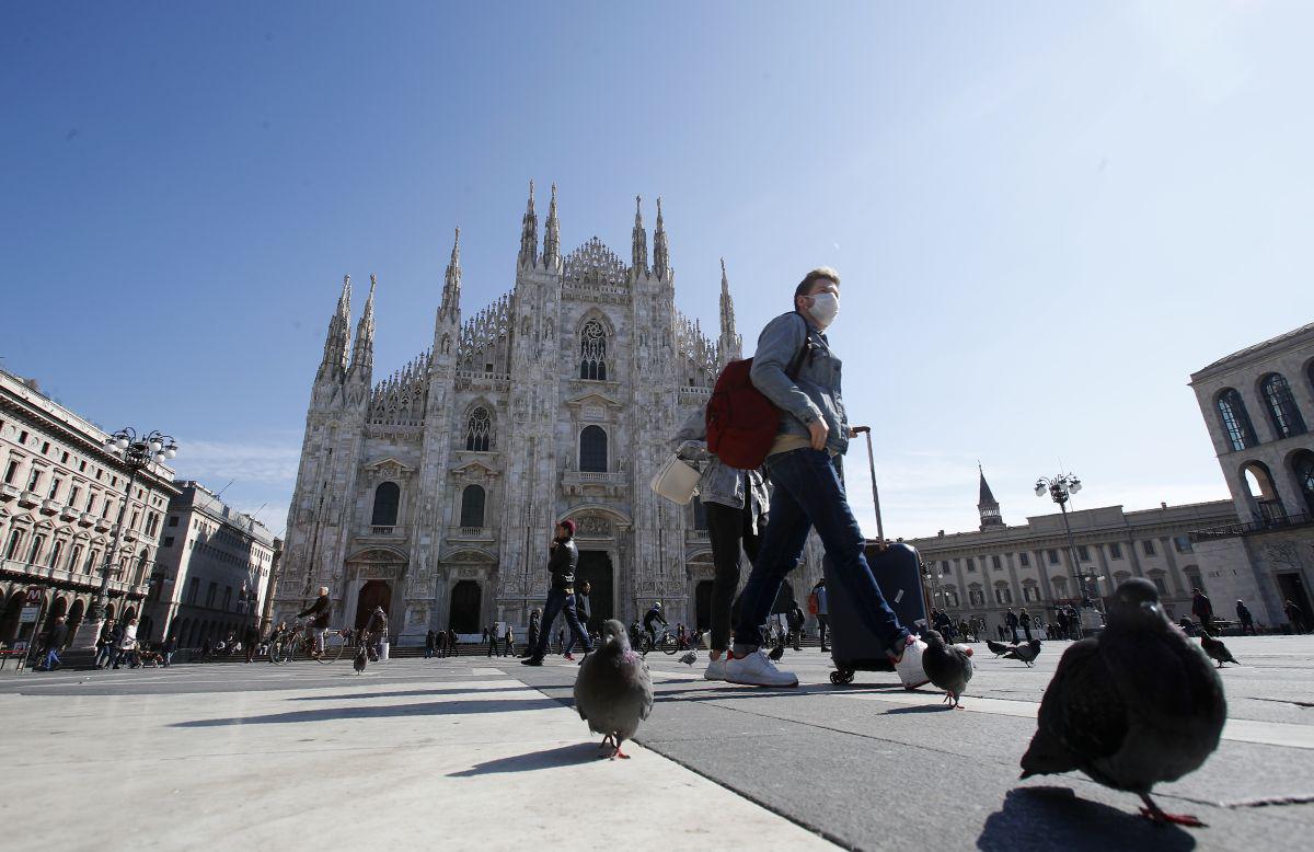 Un hombre usa una máscara mientras camina con su maleta frente a la cátedra del Duomo, en el centro de Milán, Italia. (Foto: AP)