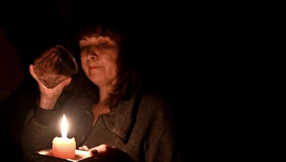 Esta fotografía tomada el 5 de noviembre de 2022 muestra a Iren Rozdobudko, una escritora y profesora universitaria de 60 años, bebiendo un vaso de agua a la luz de las velas durante un corte de energía en el edificio al norte de la capital ucraniana de Kiev. (Foto de Serguéi SUPINSKY / AFP)
