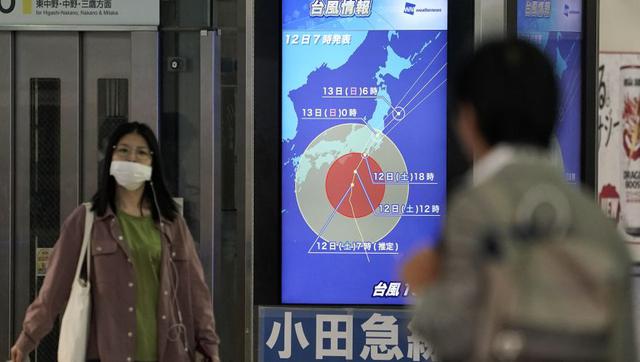 Los pasajeros del ferrocarril pasan junto a una pantalla que muestra información sobre el tifón Hagibis en la estación de tren Shinjuku. (Foto: EFE).