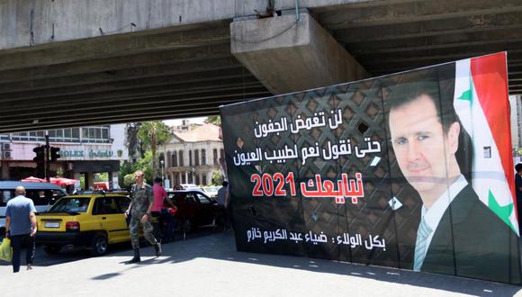 Varios peatones pasa junto a un cartel electoral que muestra al presidente de Siria, Bashar Al Asad, en la víspera de las elecciones presidenciales. (EFE/YOUSSEF BADAWI).