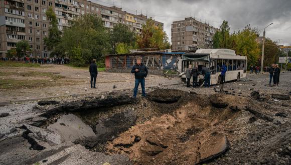 Los investigadores examinan un cráter y un autobús dañado, luego de un ataque con misiles en Dnipro el 10 de octubre de 2022, en medio de la invasión rusa de Ucrania. (Foto de Dimitar DILKOFF / AFP)