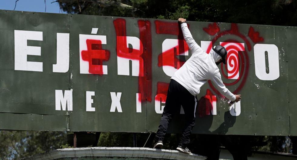 Un estudiante de Ayotzinapa pinta consignas en la entrada del Campamento Militar 1 durante una manifestación en la Ciudad de México, el 23 de septiembre de 2022. (ALFREDO ESTRELLA / AFP).