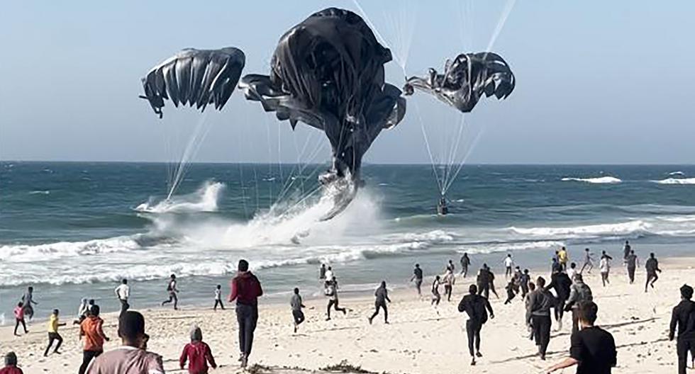 Palestinos corren hacia paracaídas que sujetan paquetes de alimentos lanzados desde aviones estadounidenses en una playa en la Franja de Gaza el 2 de marzo de 2024. (Foto de AFP).
