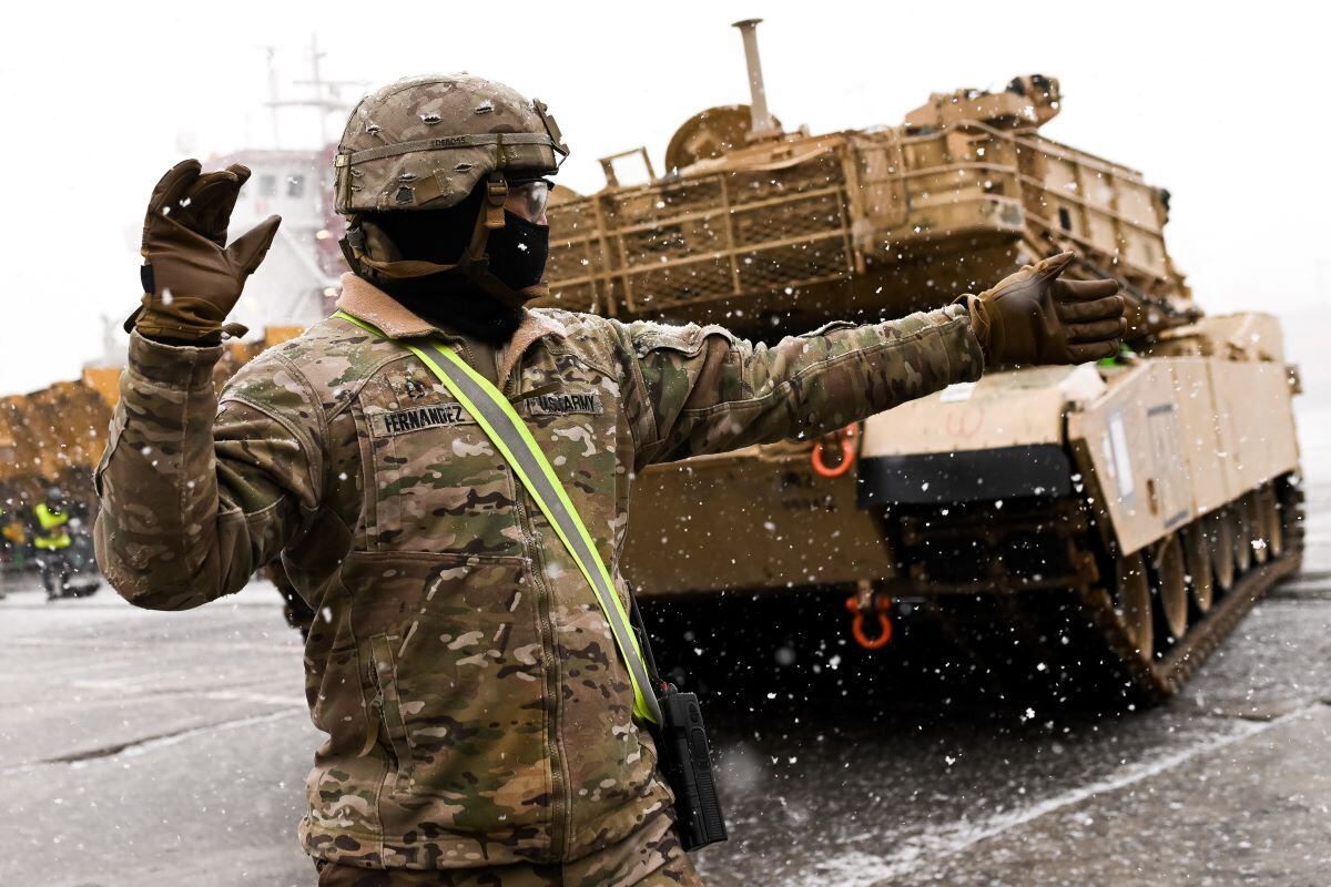 A US Army soldier points the way to an M1A2 Abrams main battle tank that will be used in military exercises.  (MATEUSZ SLODKOWSKI / AFP).