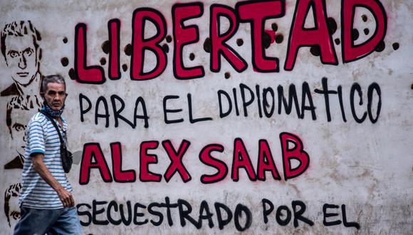 En esta foto de archivo tomada el 23 de febrero de 2021, un hombre pasa junto a un grafiti en Caracas que dice "Libertad para el diplomático Alex Saab, secuestrado por el gobierno de Cabo Verde". (YURI CORTEZ / AFP).