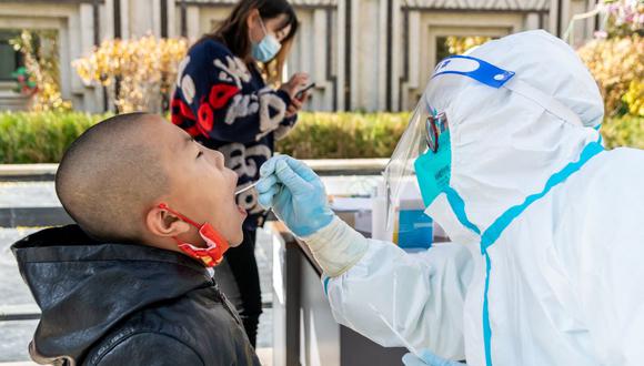 Esta foto tomada el 1 de noviembre de 2021 muestra a un trabajador médico tomando una muestra de coronavirus Covid-19 a un niño en el distrito de Ganzhou, en Zhangye, noroeste de China. (STR / AFP).