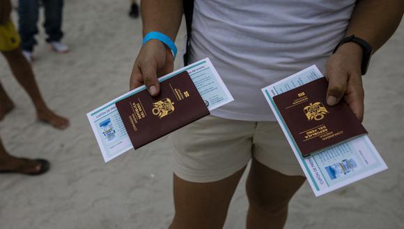 Una peruana sostiene pasaportes mientras espera en la fila para recibir la vacuna Johnson & Johnson contra el coronavirus Covid-19 en un centro de vacunación en la playa, en South Beach, Florida, el 9 de mayo de 2021. (Foto de Eva Marie UZCATEGUI / AFP).