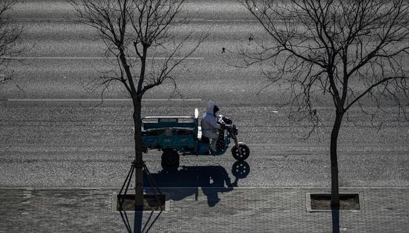 Un hombre con traje de equipo de protección personal (EPP) monta un triciclo eléctrico en una calle en medio de la pandemia de covid-19 en Beijing el 1 de diciembre de 2022. (Foto de WANG Zhao / AFP)