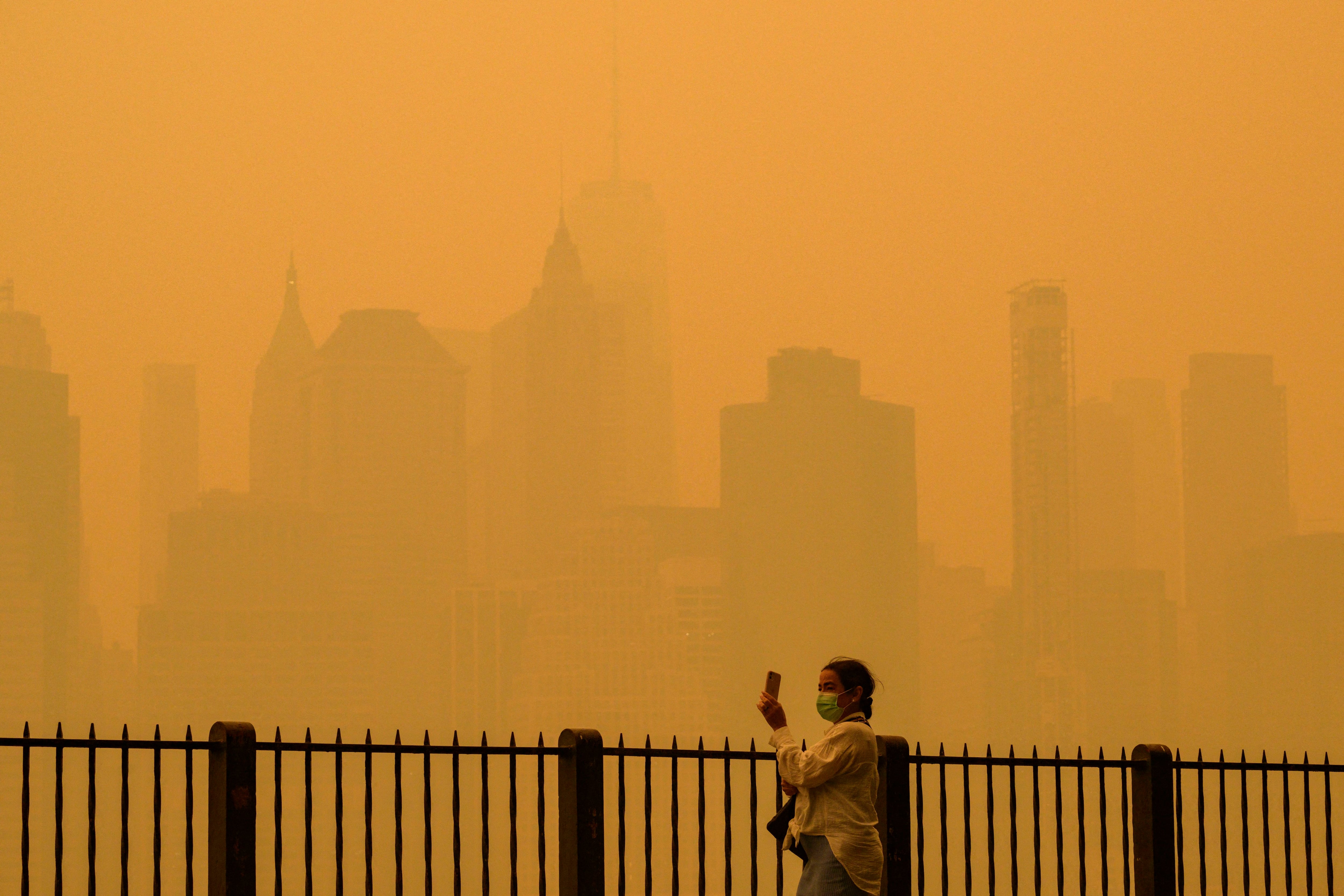 A person wearing a face mask takes photos of the skyline as smoke from wildfires in Canada causes foggy conditions in New York City on June 7, 2023. (Photo by ANGELA WEISS/AFP)