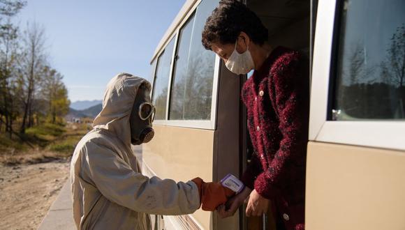 En esta foto de archivo tomada el 29 de octubre de 2020, un "funcionario de higiene y antiepidemia" verifica el calor corporal de una viajera como parte de las medidas preventivas contra el coronavirus COVID-19 en Corea del Norte. (KIM WON JIN / AFP).