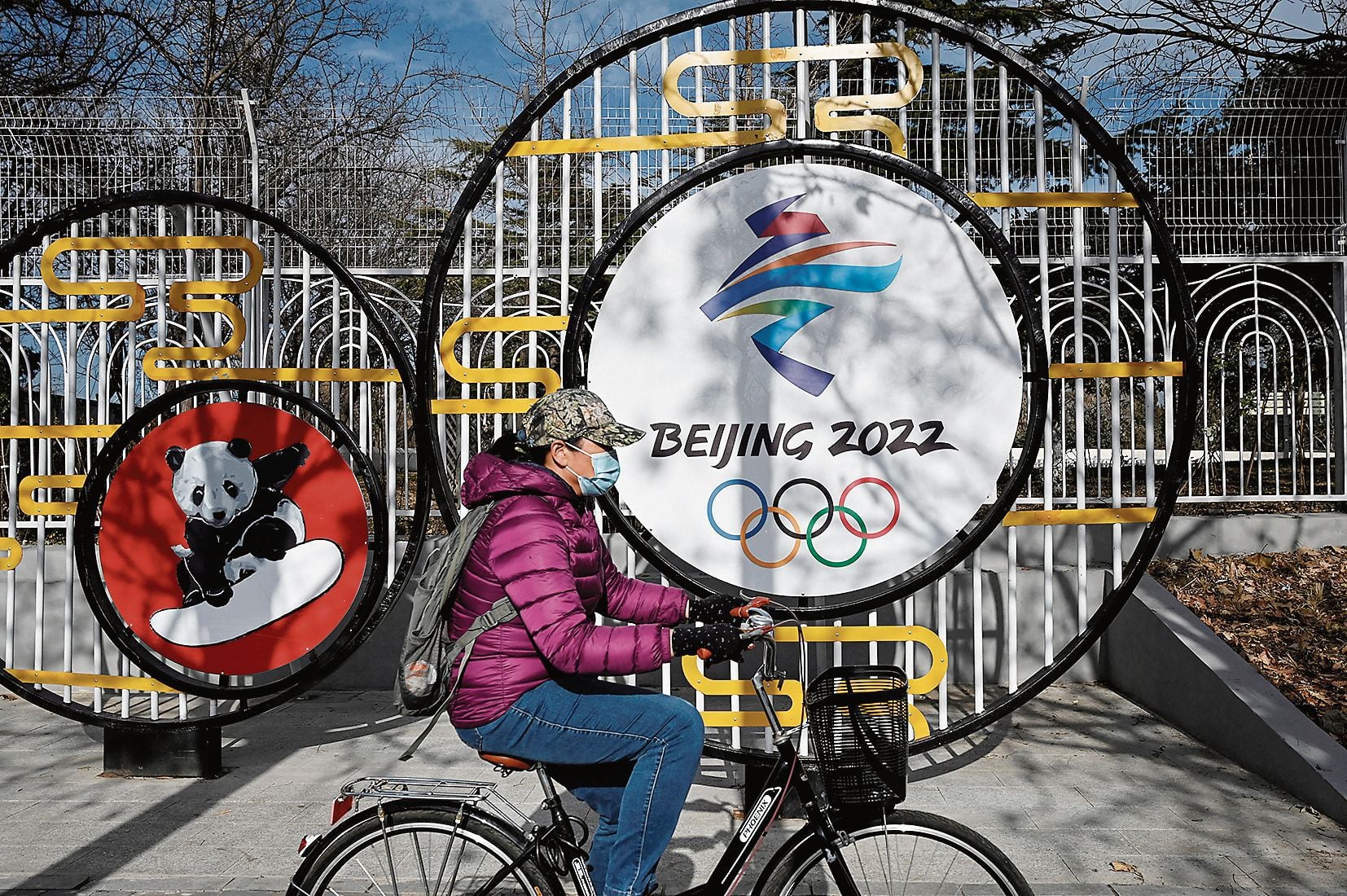 A woman rides past the Beijing 2022 Winter Olympic Games logo on a street in Beijing on December 11, 2021. (Photo by JADE GAO / AFP)