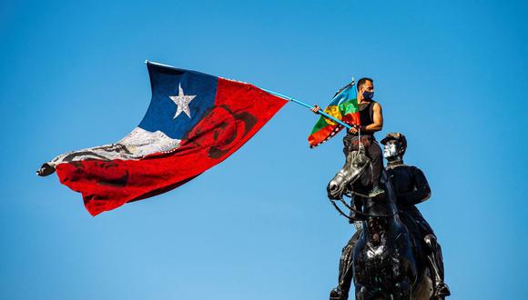 Un manifestante agita banderas chilena y mapuche desde lo alto del monumento al General Baquedano en la Plaza Italia el 9 de octubre de 2020. (Martín BERNETTI / AFP).