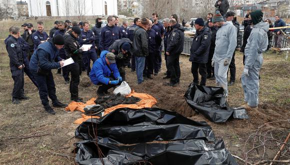 Investigadores forenses franceses, que llegaron a Ucrania para investigar crímenes de guerra en medio de la invasión rusa, observan cómo colegas ucranianos exploran restos de cuerpos de civiles quemados exhumados de una tumba en la ciudad de Bucha. (REUTERS/Valentyn Ogirenko)