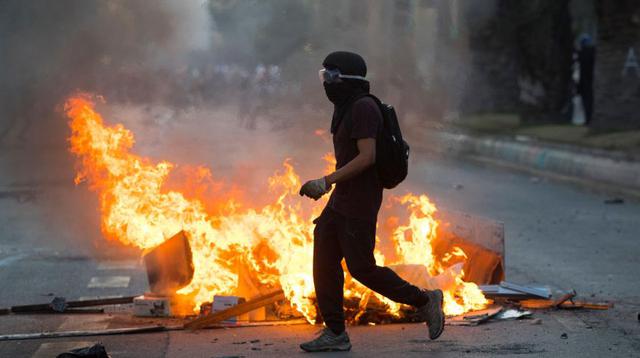 Un hombre camina junto a una barricada en llamas en la Plaza Italia. (Foto: EFE)