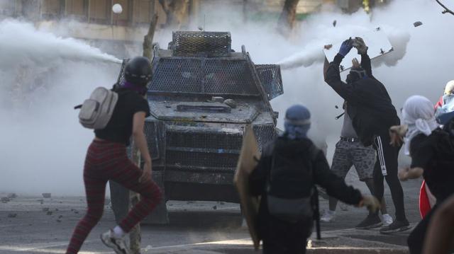 Manifestantes antigubernamentales chocan con un vehículo blindado de la policía que arroja gases lacrimógenos durante las protestas en Santiago. (Foto: AP).