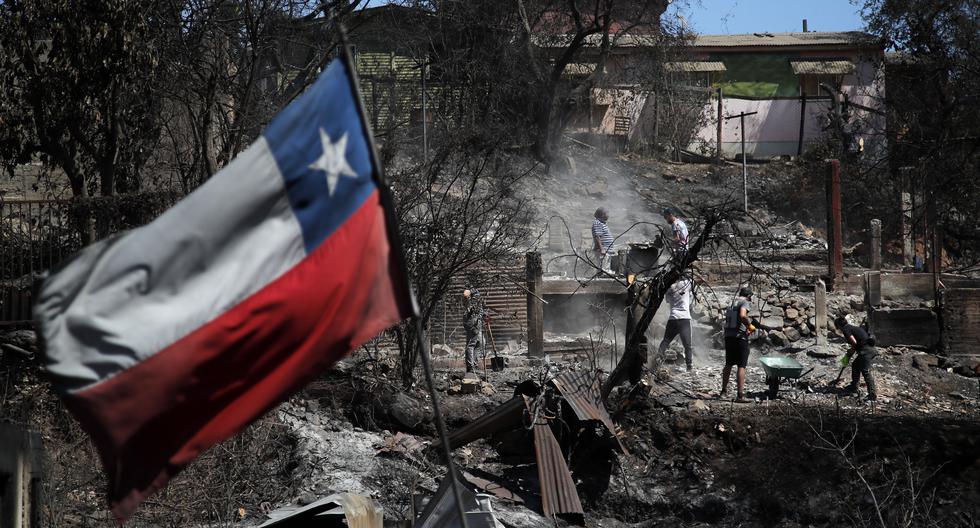 Una bandera de Chile ondea mientras los vecinos inspeccionan casas quemadas en Villa Independencia, región de Valparaíso, el 5 de febrero de 2024. (Foto de Javier TORRES/AFP).