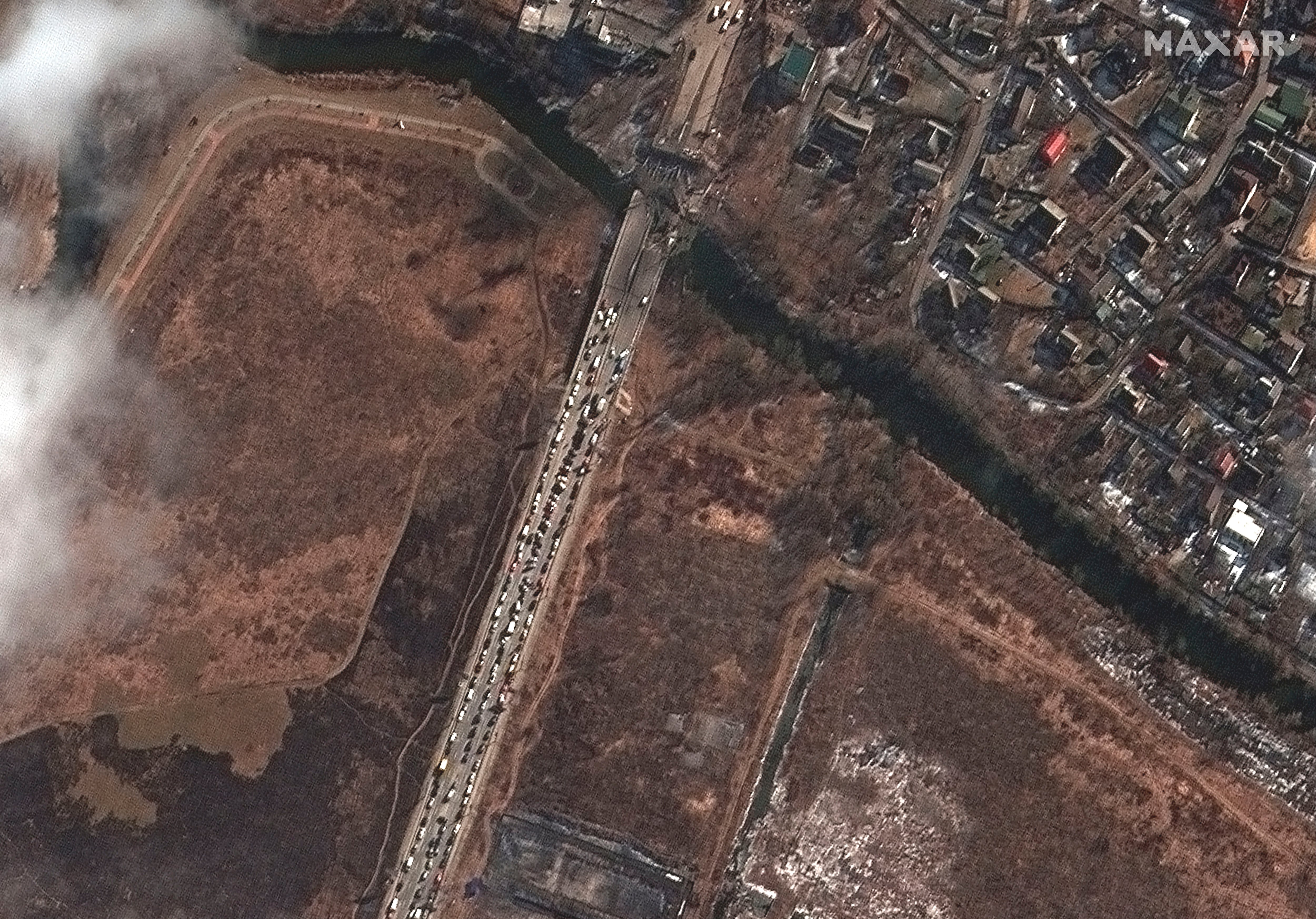 A long line of people and cars waiting by the damaged Irpin River bridge during the Russian invasion, in Irpin, Ukraine.  (Satellite image ©2022 Maxar Technologies via AP.)