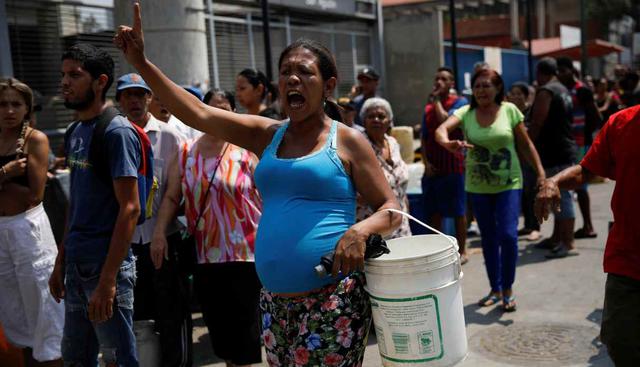 La gente grita mientras hacen cola para tratar de recolectar agua en una calle de Caracas. (Foto: Reuters)