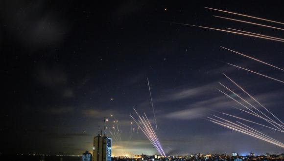 En el fondo, el sistema israelí de defensa antimisiles Cúpula de Hierro (izquierda) intercepta cohetes disparados por el movimiento Hamas hacia el sur de Israel desde Beit Lahia, en el norte de la Franja de Gaza. (Foto de ANAS BABA / AFP).