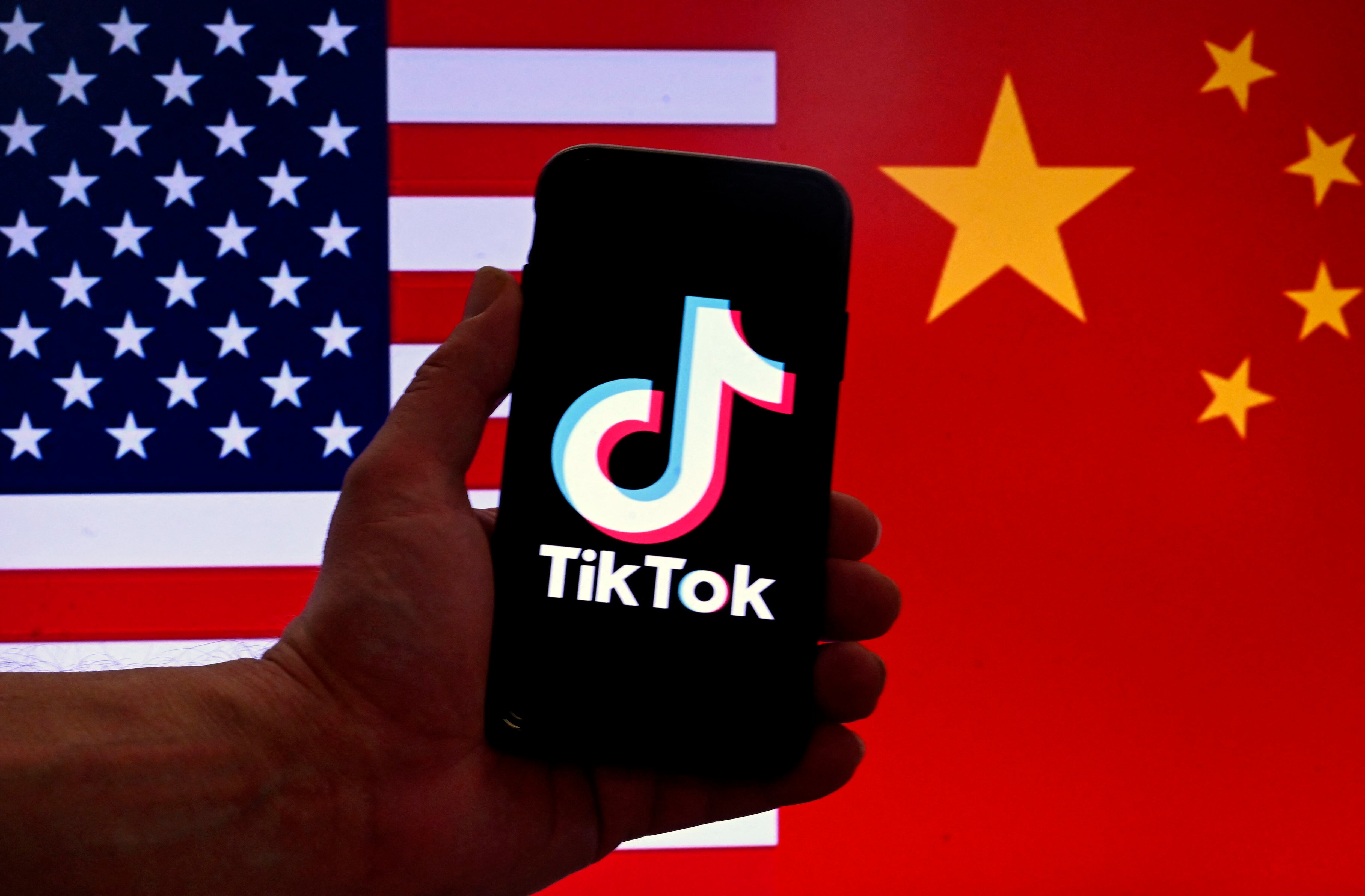 In this photo illustration, the logo for the social media app TikTok is displayed on an iPhone screen in front of an American flag and a Chinese flag.  (Photo by OLIVIER DOULIERY/AFP).