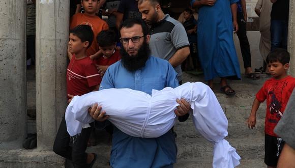 Un pariente lleva el cuerpo de un niño de la familia de Abu Quta. Diecinueve  integrantes de que misma familia murieron en los ataques israelíes contra la ciudad palestina de Rafah, en el sur de la Franja de Gaza. (Foto de SAID KHATIB / AFP).