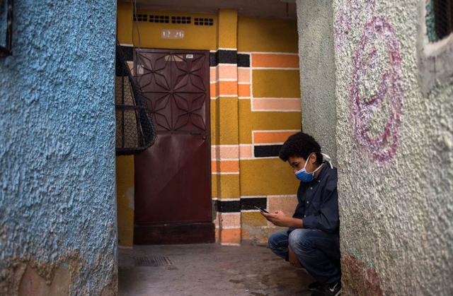 Jonathán Figueroa, de 14 años, usa su teléfono celular, conectado a la señal wifi de un vecino, frente a su casa en el barrio Bello Campo en Chacao, Caracas (Venezuela), el 6 de octubre de 2020, en medio de la pandemia de coronavirus. (AFP / Cristian Hernandez).