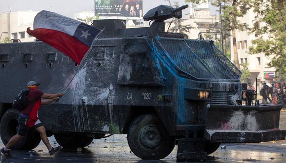Un manifestante se acerca a un vehículo de la policía de Chile durante una protesta en Santiago. (AFP / Claudio REYES).