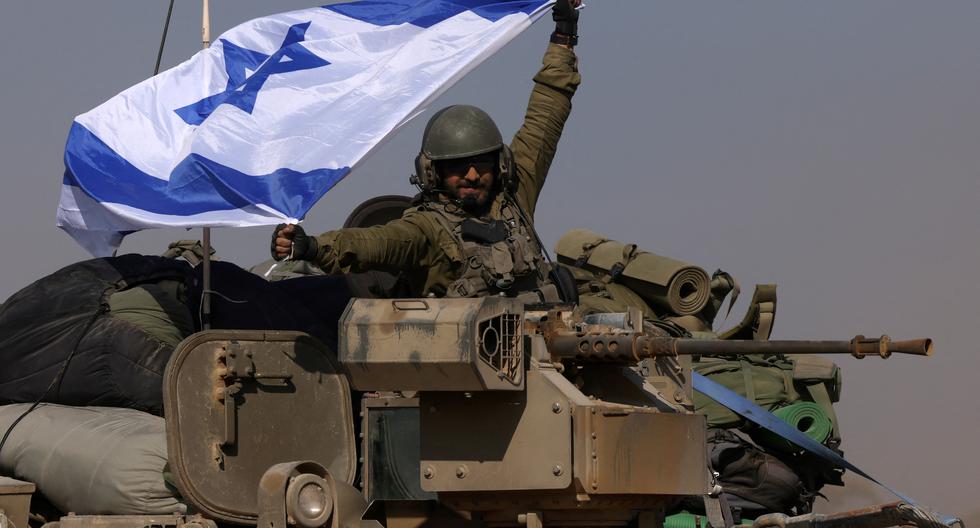 Esta fotografía tomada cerca de la frontera con la Franja de Gaza muestra a un soldado israelí en un vehículo blindado de transporte de tropas (APC) ondeando una bandera israelí mientras las tropas retroceden desde la Franja de Gaza, el 31 de diciembre del 2023. (Foto: AFP)