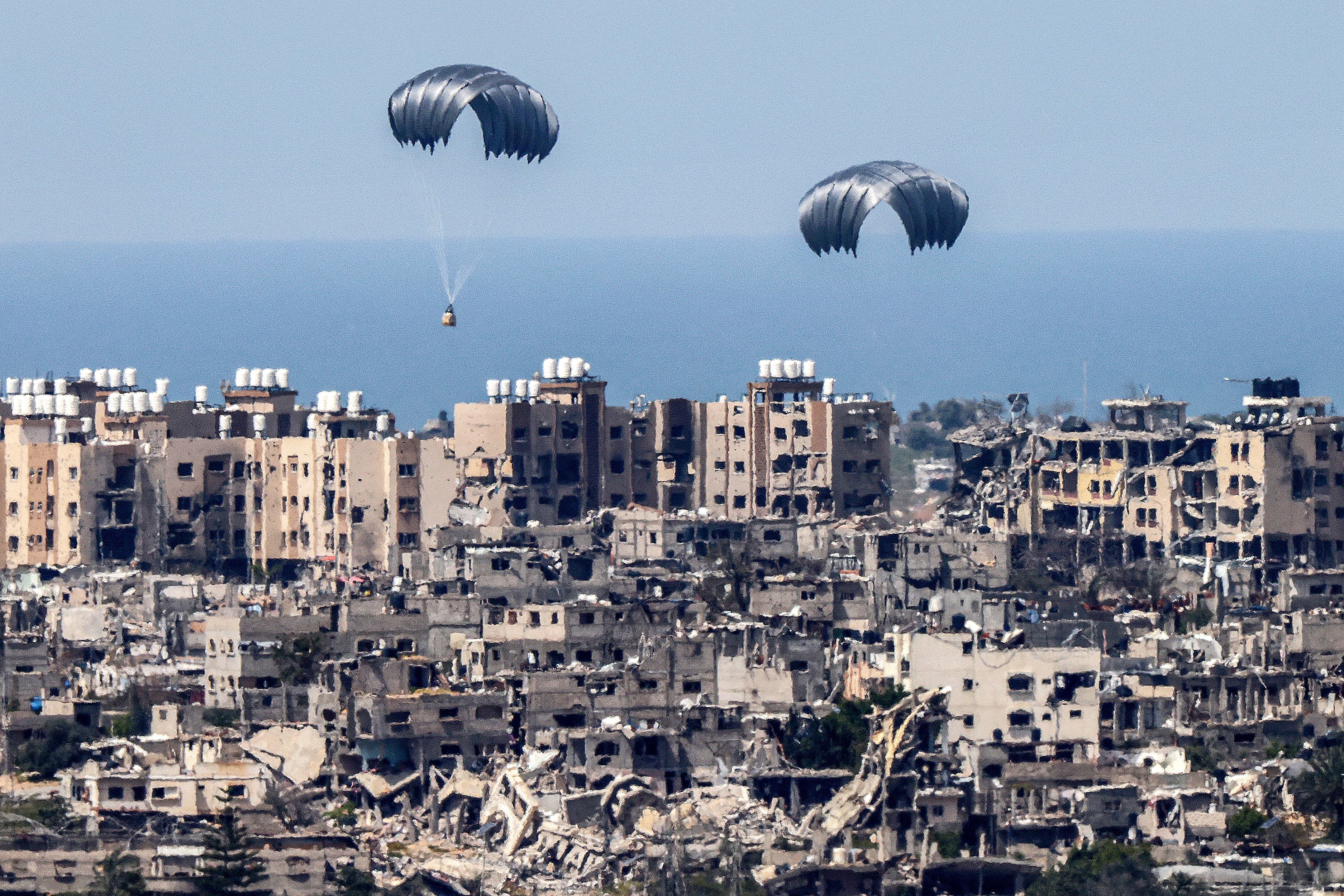 This photograph taken from Israel's southern border with the Gaza Strip shows humanitarian aid parachutes landing in the besieged Palestinian territory on March 26, 2024. (Photo by JACK GUEZ/AFP).