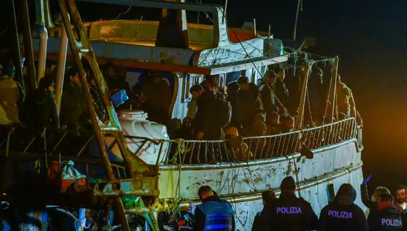 Varios policías, abajo, aguardan frente a un barco pesquero con unos 500 migrantes la madrugada del sábado 11 de marzo de 2023 en el puerto de Crotone, en el sur de Italia.
