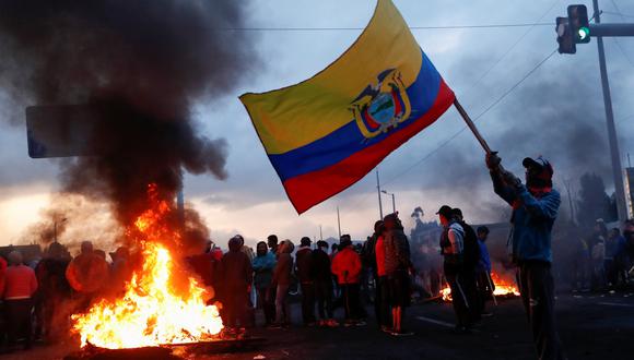 Un hombre ondea una bandera ecuatoriana junto a numerosos manifestantes que bloquean una carretera cerca de Quito durante las protestas contra el gobierno de Lenín Moreno. (REUTERS / Carlos Garcia Rawlins).