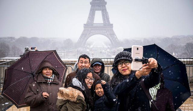 People pose for selfies under the snow on the Place du Trocadero in front the Eiffel Tower in Paris on February 5, 2018. / AFP / Lionel BONAVENTURE