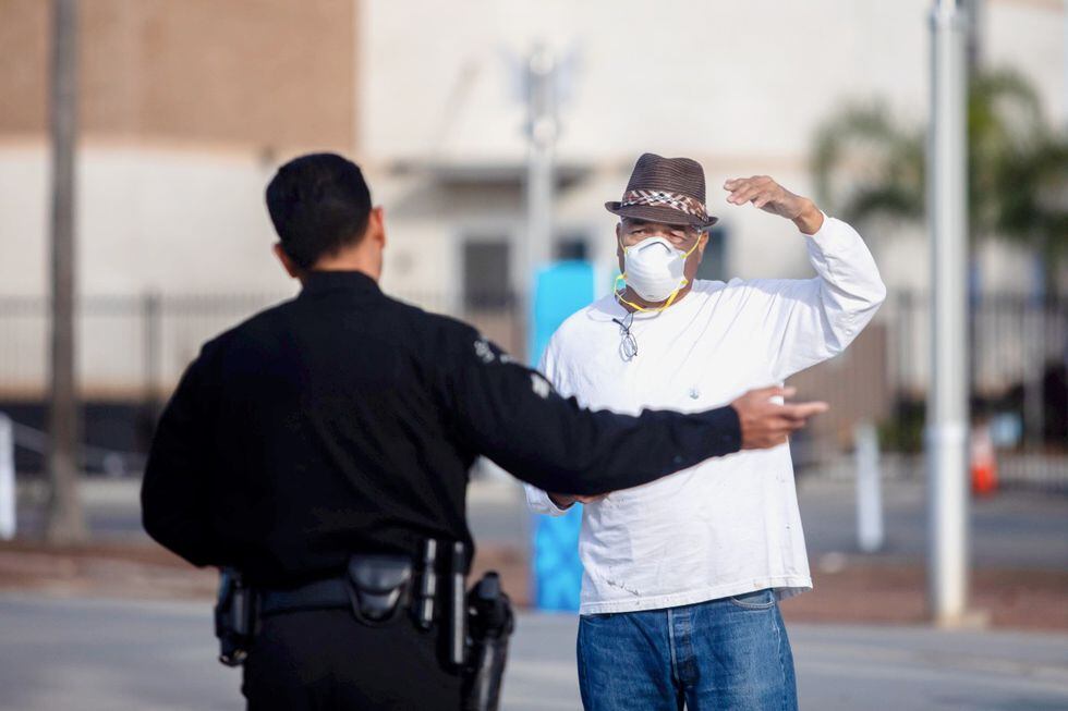 Un oficial de policía habla con un hombre que lleva una mascarilla como medida preventiva contra el coronavirus. Foto del  28 de marzo de 2020 en el Puerto de Los Ángeles en San Pedro, California. AFP / Apu GOMES