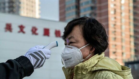 En la imagen, un guardia de seguridad verifica la temperatura de una mujer que usa una máscara protectora como medida preventiva después del brote del coronavirus. (Foto: AFP)