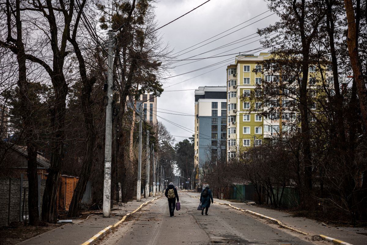 A couple walk down a street as they flee from the city of Irpin, northwest of Kiev, on March 13, 2022. (DIMITAR DILKOFF / AFP)