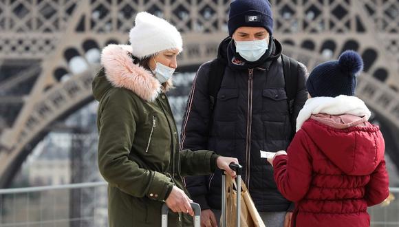 Un grupo de personas usan una máscara protectora mientras caminan frente a la torre Eiffel, en París, mientras el país sufre un duro brote del COVID-19. (AFP)
