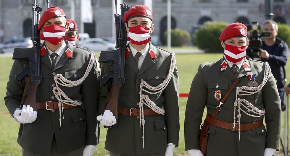 Guardias austríacos, con mascarillas alusivas a la bandera del país, durante una ceremonia militar en el 75 aniversario del restablecimiento de la República de Austria, en abril del 2020. 
 (AP Photo/Ronald Zak)
